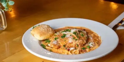 Plated chicken parmesan over fettuccine with garlic bread on a wooden table