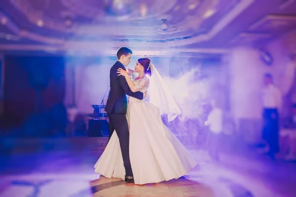 A bride and groom dancing at a wedding reception under purple stage lighting and smoke effects.