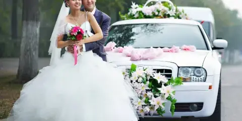 Bride and groom posing in front of a white wedding car decorated with flowers