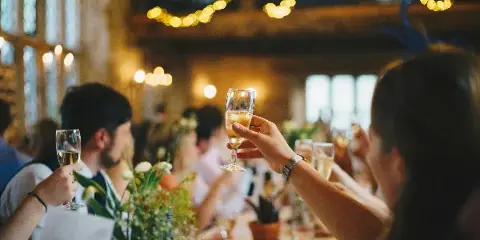 Guests at a wedding reception table raising champagne glasses in a toast.