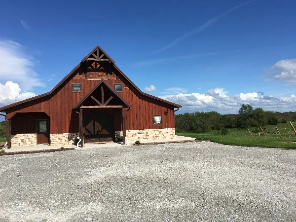 Exterior view of a red wooden barn event center with a stone foundation and gravel parking area.