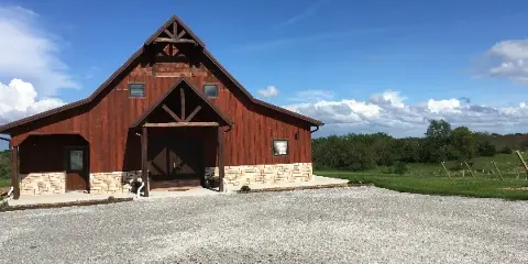 Exterior view of a red wooden barn event center with a stone foundation and gravel parking area.