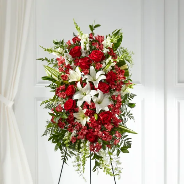 A tall, vertical floral arrangement featuring red roses, white lilies, and greenery on a tripod stand.