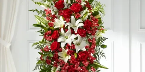 A tall, vertical floral arrangement featuring red roses, white lilies, and greenery on a tripod stand.