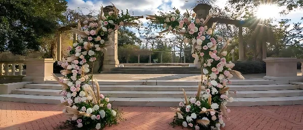 A large outdoor floral archway decorated with pink and white roses and pampas grass.