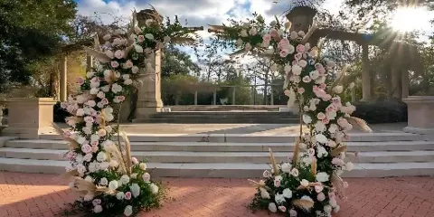 A large outdoor floral archway decorated with pink and white roses and pampas grass.