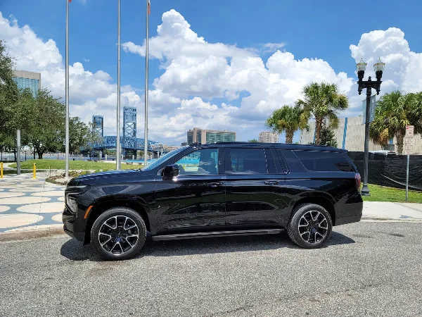 A black luxury SUV parked on a street with a blue bridge and city buildings in the background.