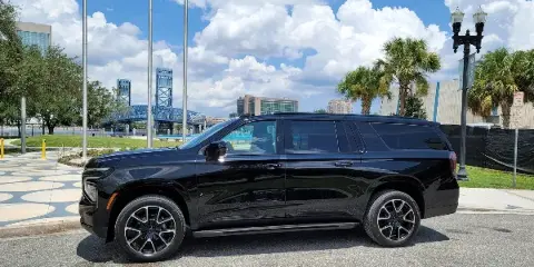 A black luxury SUV parked on a street with a blue bridge and city buildings in the background.