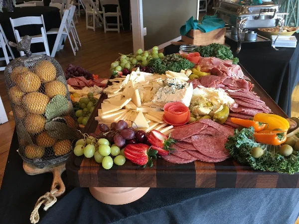 A catering table featuring a large charcuterie board with meats, cheeses, and fruits, set in an event venue.