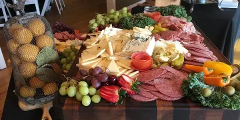 A catering table featuring a large charcuterie board with meats, cheeses, and fruits, set in an event venue.