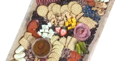 A wooden tray filled with an assortment of charcuterie meats, cheeses, crackers, dried fruit, and fresh berries.