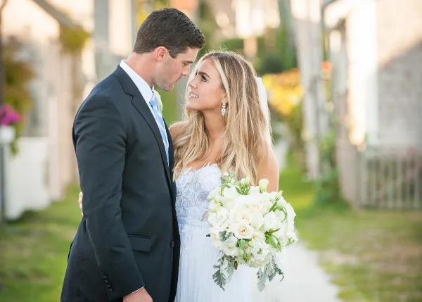 A bride and groom standing close together outdoors, with the bride holding a white bouquet.