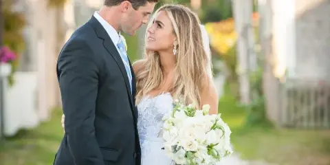 A bride and groom standing close together outdoors, with the bride holding a white bouquet.