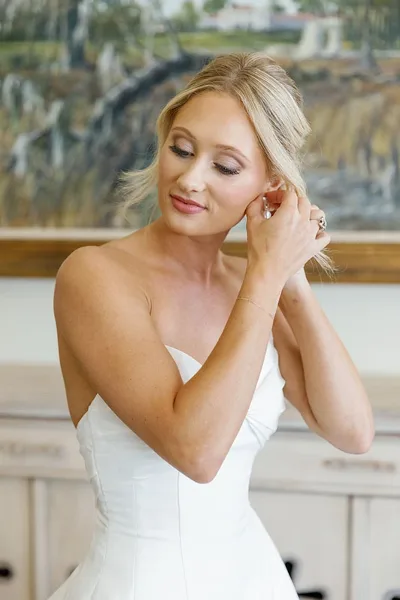 A bride with styled hair and makeup adjusting her earring.