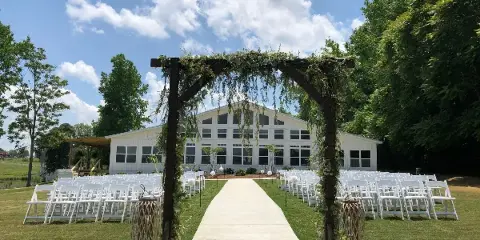 Outdoor wedding ceremony setup with a wooden arch, white chairs, and a large white venue building in the background.