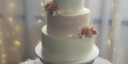 A three-tiered white wedding cake with pink floral decorations and a Mr & Mrs topper on a metal stand.