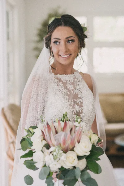 Bride with styled updo, makeup, veil, and floral bouquet