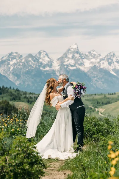 Bride and groom kissing in a field with the Grand Teton mountains in the background