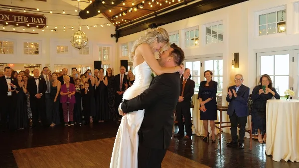 A bride and groom share a kiss during their first dance at a wedding reception while guests applaud.
