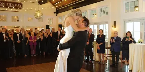 A bride and groom share a kiss during their first dance at a wedding reception while guests applaud.