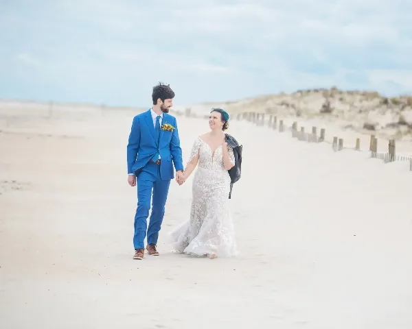A bride and groom holding hands and walking on a sandy beach.