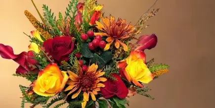A vibrant floral arrangement with red and yellow roses, orange chrysanthemums, and greenery in a clear glass vase.