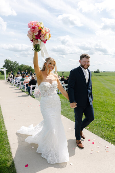 A bride and groom walking down a wedding aisle outdoors.