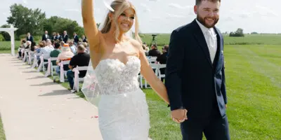 A bride and groom walking down a wedding aisle outdoors.