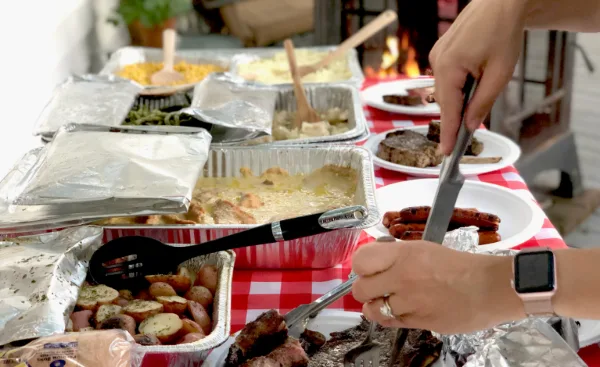 A catering table with various food trays and people serving themselves.