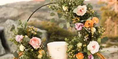 A wedding reception table centerpiece featuring a floral arch with roses and greenery surrounding a white cake.