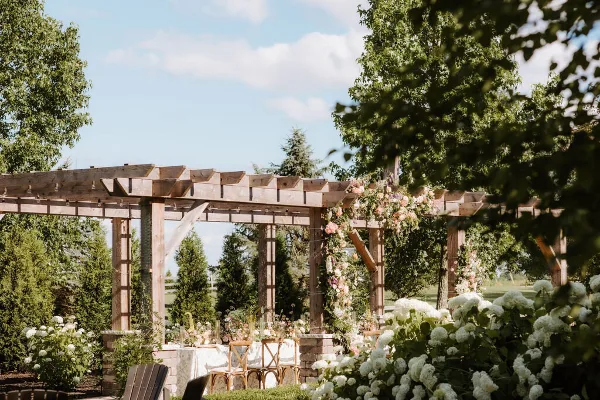 Outdoor wedding ceremony area with a wooden pergola decorated with flowers and chairs set up under a clear sky.