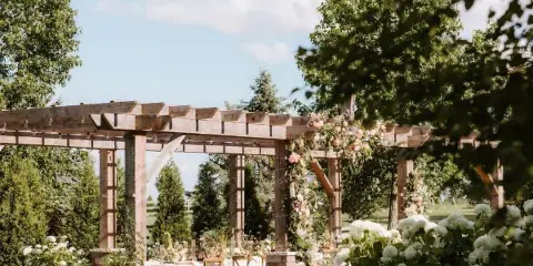 Outdoor wedding ceremony area with a wooden pergola decorated with flowers and chairs set up under a clear sky.