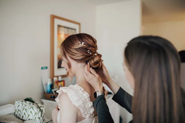 A hair stylist styling an intricate updo on a bride.