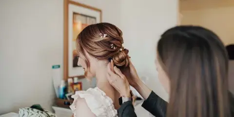 A hair stylist styling an intricate updo on a bride.