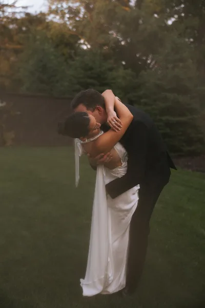 A bride and groom embracing in a grassy outdoor setting.
