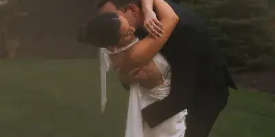A bride and groom embracing in a grassy outdoor setting.