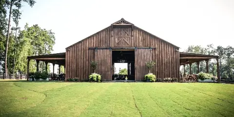 A large wooden barn with open doors and covered outdoor seating areas on a green lawn.