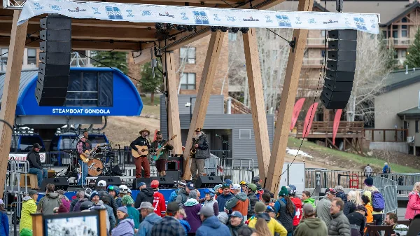 A band performing on an outdoor stage with professional audio equipment in front of a crowd.