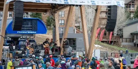 A band performing on an outdoor stage with professional audio equipment in front of a crowd.