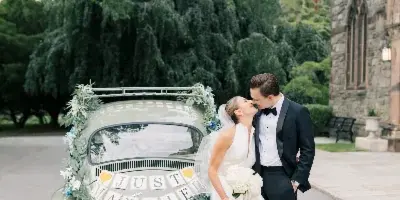 A bride and groom kissing next to a vintage car decorated with flowers and a 'Just Married' sign.
