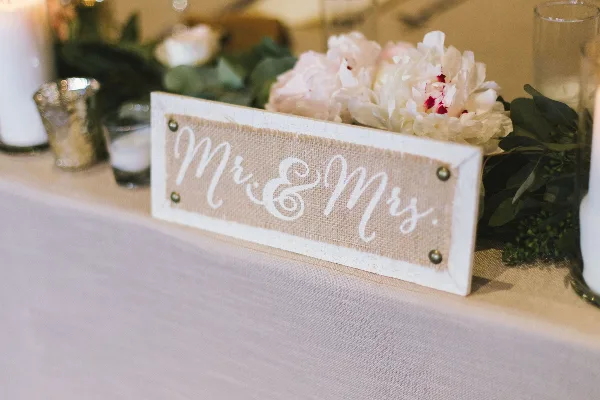A wedding table centerpiece featuring white peonies, greenery, and a rustic 'Mr & Mrs' sign.