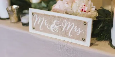 A wedding table centerpiece featuring white peonies, greenery, and a rustic 'Mr & Mrs' sign.