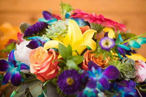 A colorful floral arrangement featuring yellow lilies, orange roses, and purple orchids.