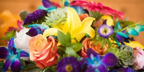 A colorful floral arrangement featuring yellow lilies, orange roses, and purple orchids.