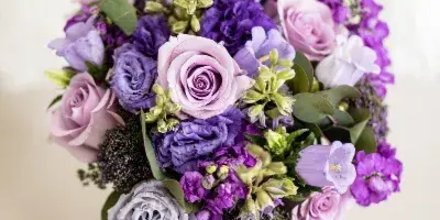 A purple and lavender bridal bouquet featuring roses, stock, and lisianthus resting on a pair of glittering high heels.