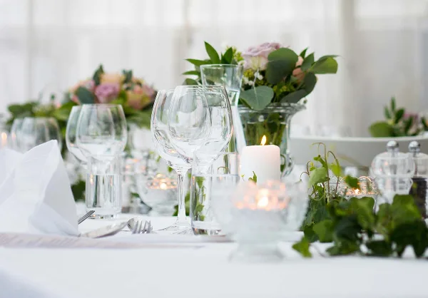 A close-up of an elegant event table setting featuring wine glasses, flatware, and floral arrangements.