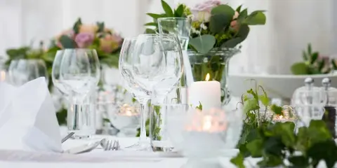 A close-up of an elegant event table setting featuring wine glasses, flatware, and floral arrangements.