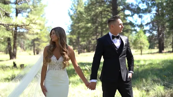 A bride and groom holding hands in a grassy outdoor area with trees in the background.