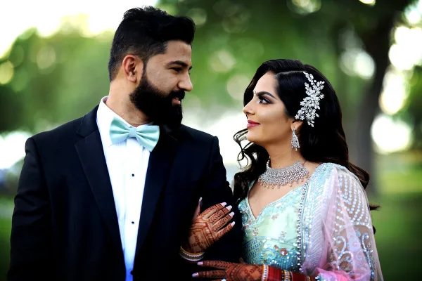 A bride and groom in formal wedding attire smiling at each other outdoors.