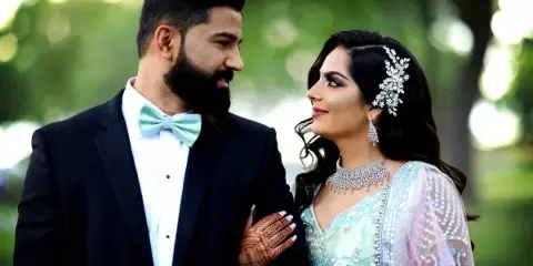 A bride and groom in formal wedding attire smiling at each other outdoors.